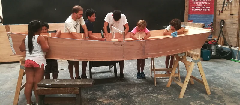 Chicos y docentes alrededor del casco de un bote en construcción