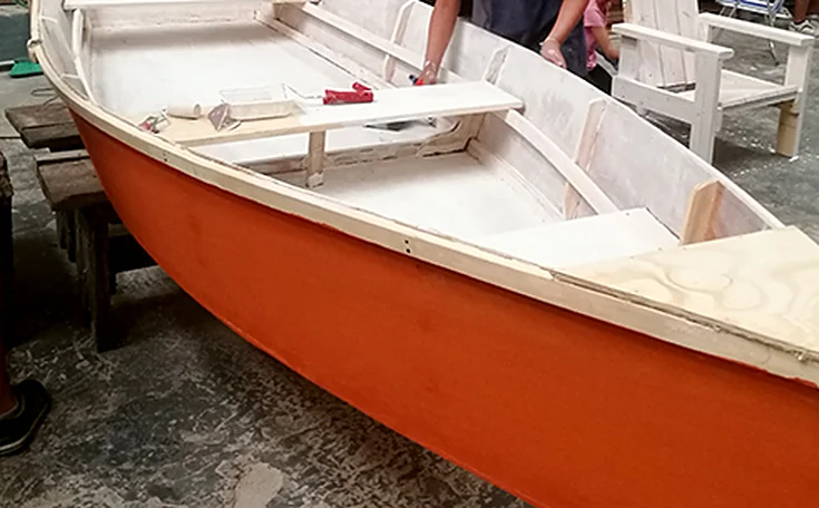 Bote de madera pintado de naranja y blanco, terminado, en el taller.