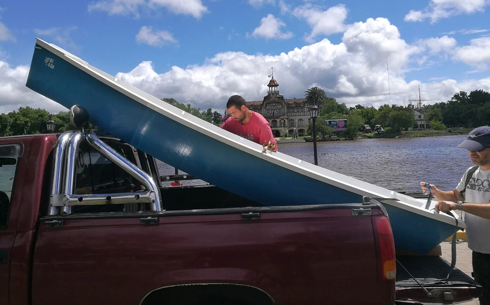 Un bote celeste cargado en la caja de una camioneta, junto a la orilla del río en Tigre.