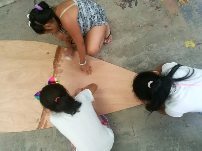 Tres chicas trazan una pieza de madera en el piso del taller